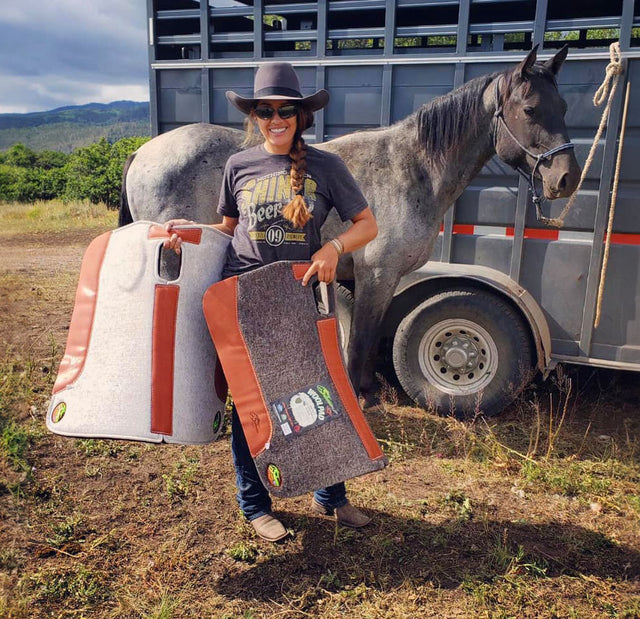 A smiling rider holding two Southwestern Equine saddle pads beside her horse